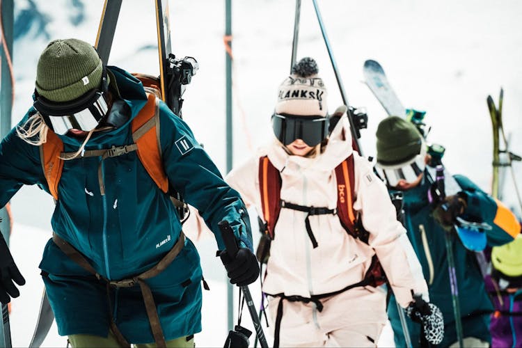 3 people carrying their skis all wearing hats and big googles