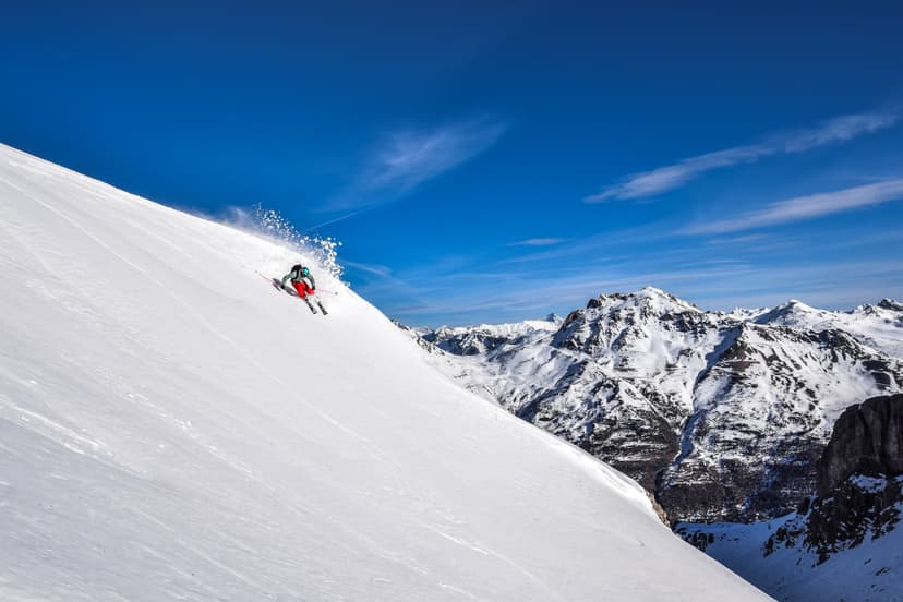 Skiier carving down off piste mountain on bluebird day