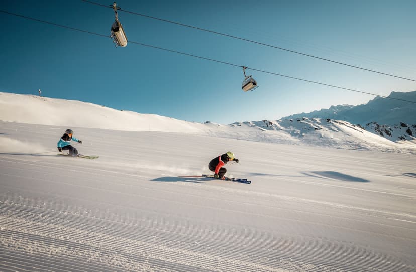 Skiers skiing fast down slope under a chairlift