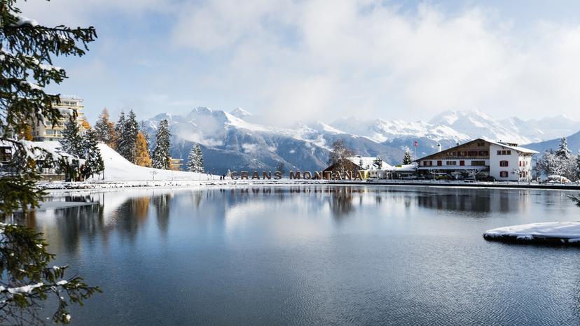 Crans Montana Ski resort sign with lake in foreground and mountains in background